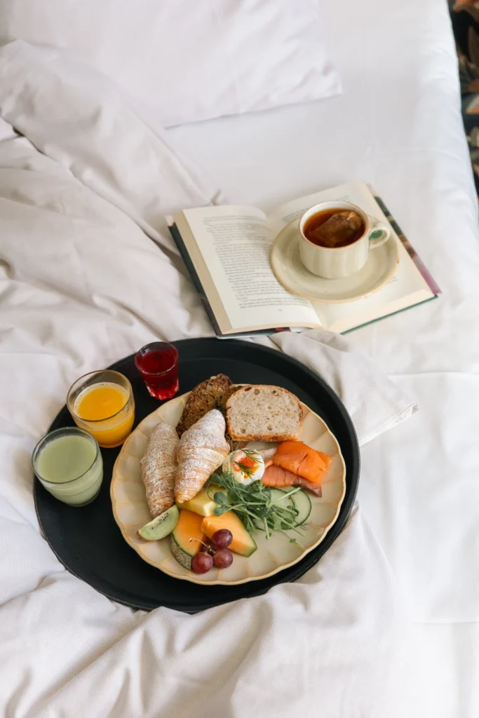 Luxurious breakfast in bed with croissants, salmon, fruit and coffee next to an open book - perfect for relaxing