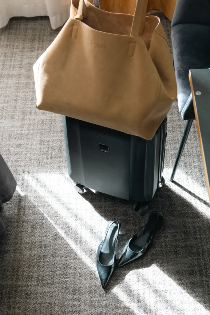 Suitcase with elegant beige handbag and black heeled shoes in hotel room, ready for spa weekend