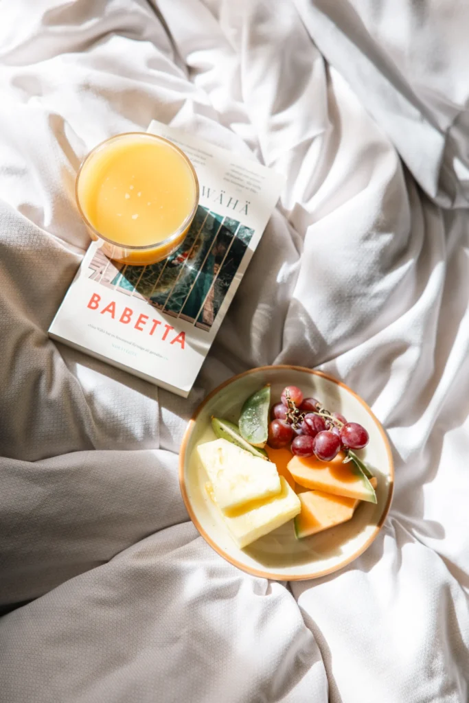 Elegant warm fruit platter with grapes and citrus and fresh orange juice served on the bed next to the book