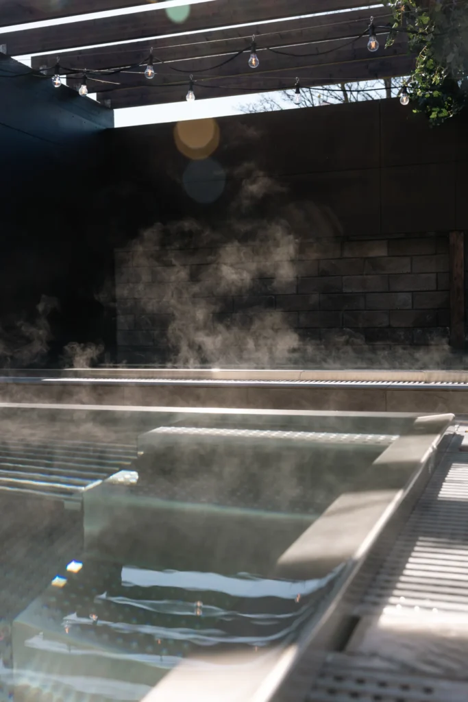 Ångande spa-pool med utsikt mot naturmiljö, omgiven av stämningsbelysning och glasräcken för avkopplande bad