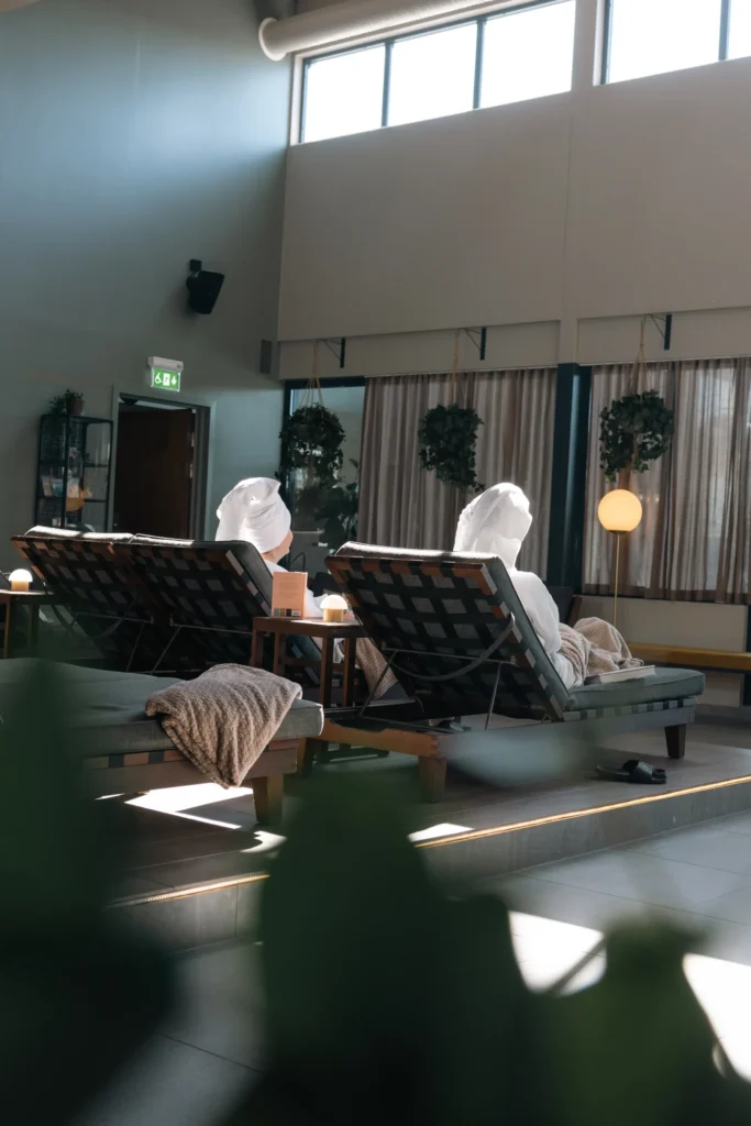 Two guests resting in sun loungers with towels in the spa's relaxation area with high ceilings and large windows