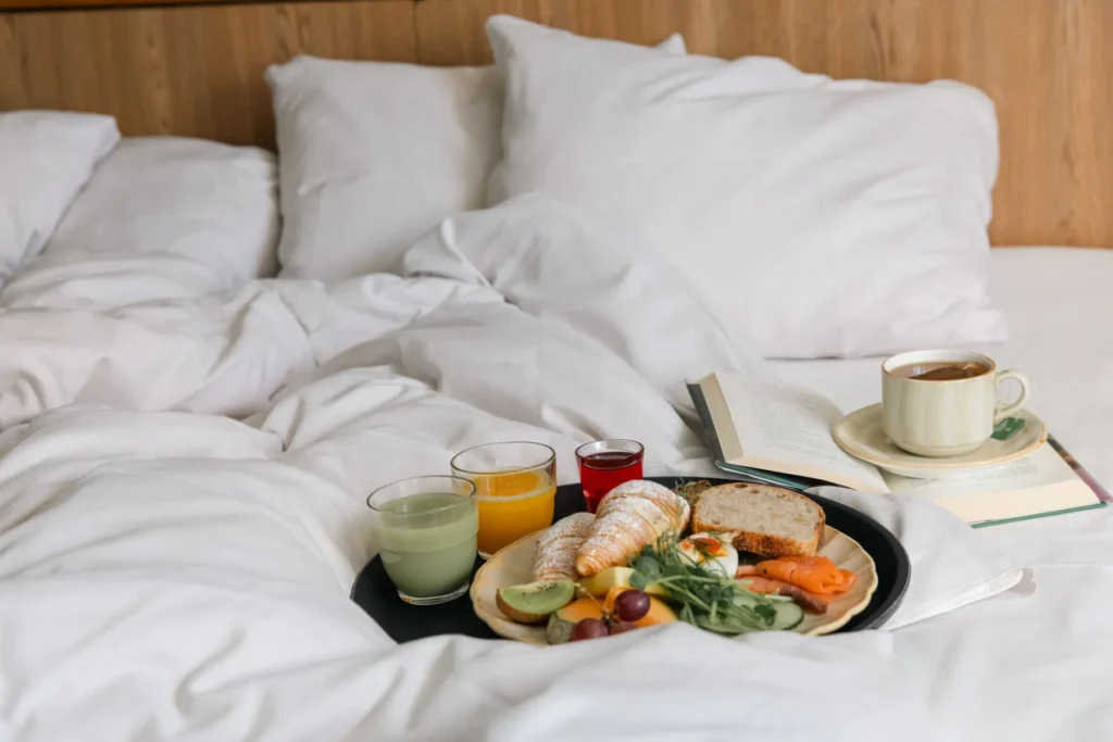 Lyxig frukost i säng med kaffe, juice, croissanter och färsk frukt på vit sängkläder