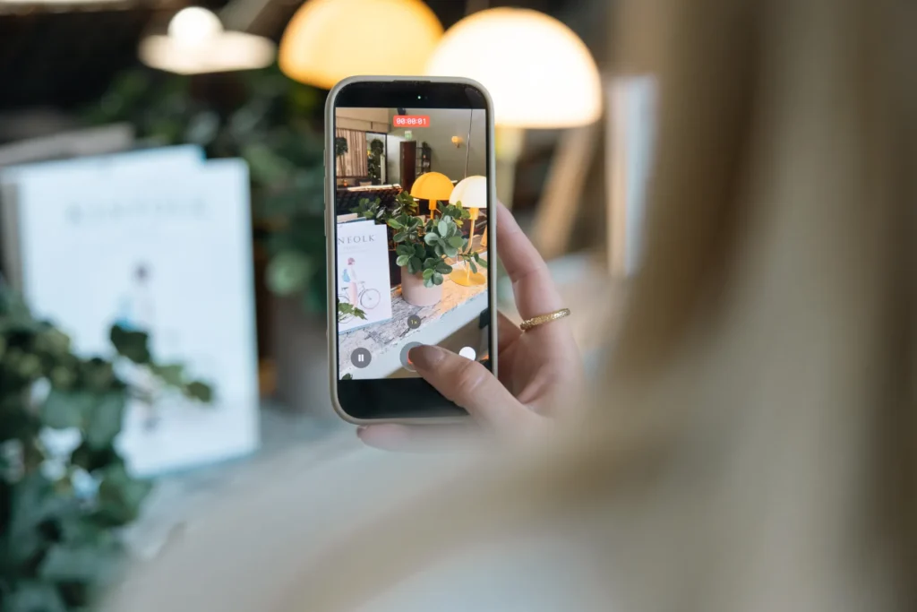Guest photographs hotel room with cell phone, showing modern lights and green plant decor in serene setting