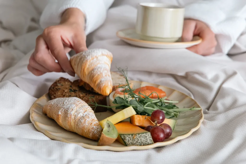 Luxurious breakfast in bed with croissants, fresh fruit, cheese and coffee served on elegant china