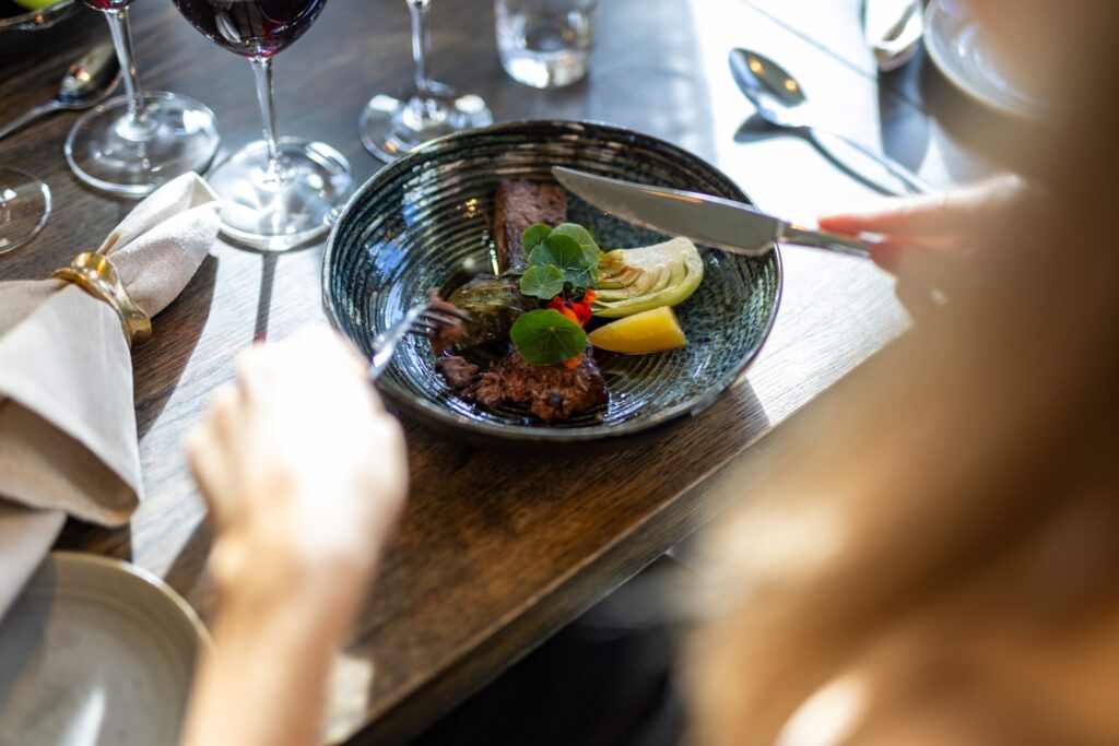 Elegant restaurangmiddag med kött i mörk skål, dekorerat med grönsaker och serverat med rödvin på bord