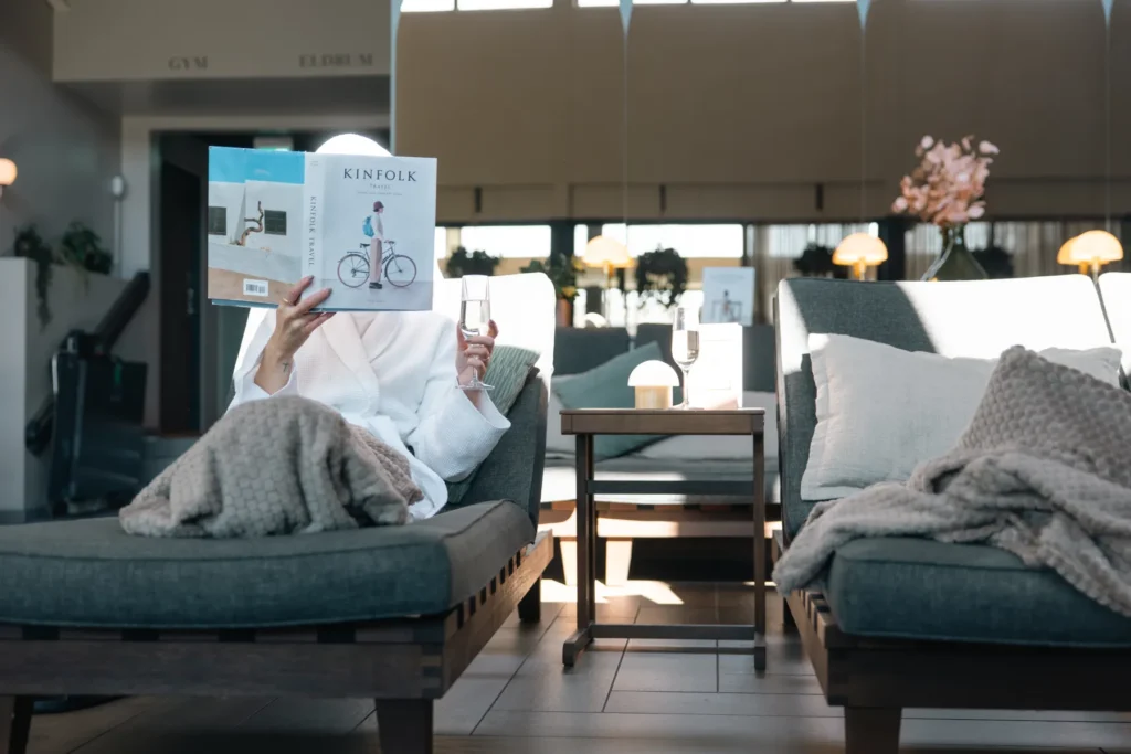 Gast liest die Zeitschrift Kinfolk in einem bequemen Sessel mit Decke und Champagner auf einem Beistelltisch in der hellen Hotellobby