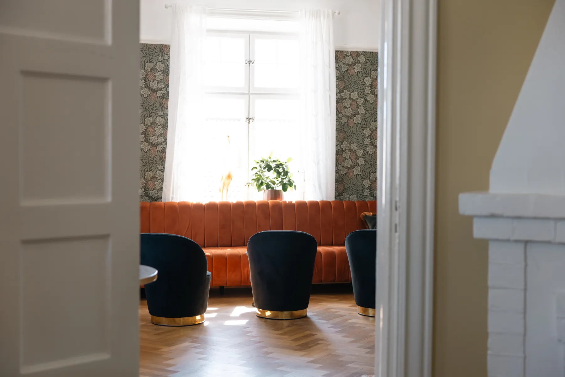 Elegant lounge med orange sammetssoffa vid fönster och svarta fåtöljer, inbjudande miljö för avkoppling
